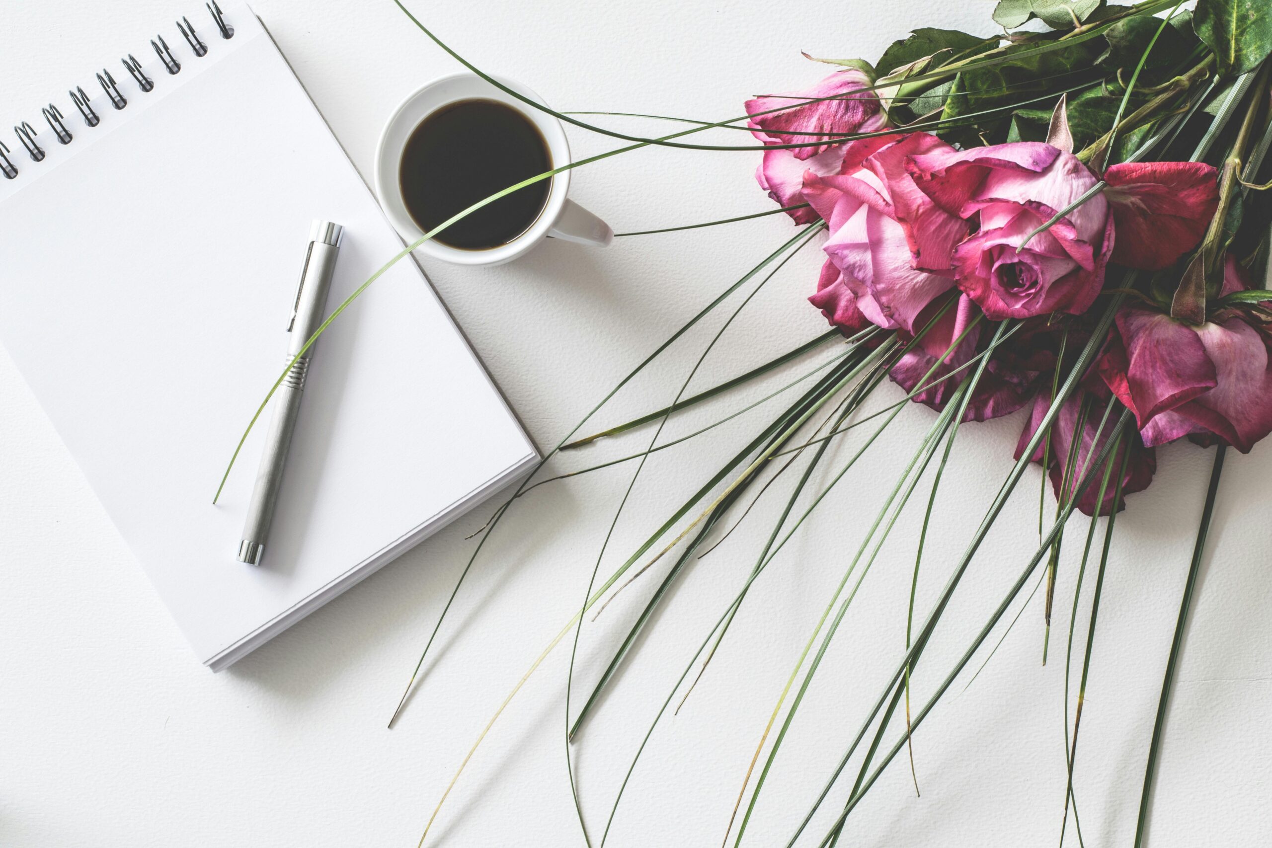 Red rose flowers bouquet on white surface beside spring book with click pen and cup of cofffee